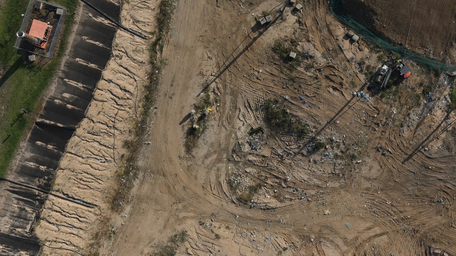 Aerial view of an active landfill cell: lined batter, haul road, waste face and excavator